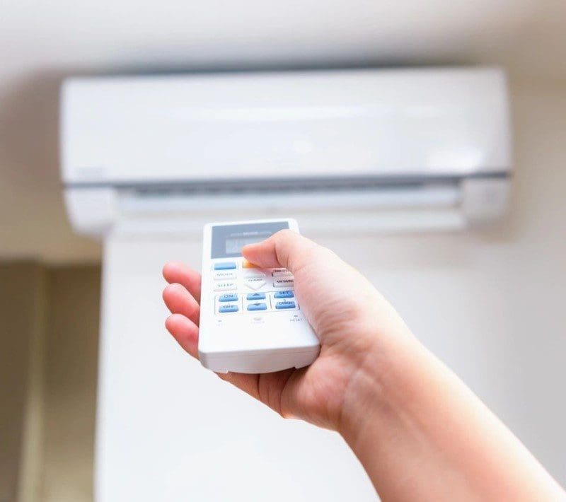A person is holding a remote control in their hand to control a residential ac unit
