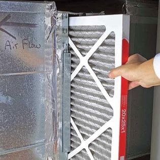 Person Touching the Air Filter on an Air Conditioner A person is inspecting and touching the air filter of an air conditioner, preparing to clean or replace it for optimal system performance