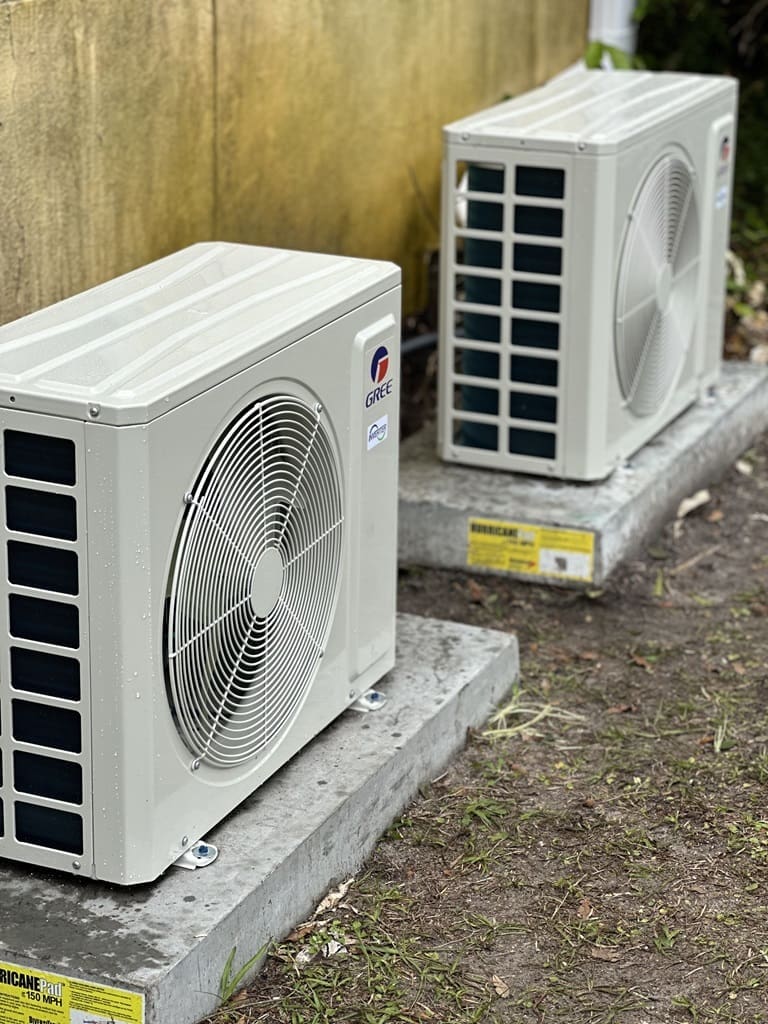 Two ductless air conditioners are installed on a concrete slab outside, positioned securely for efficient cooling and ventilation