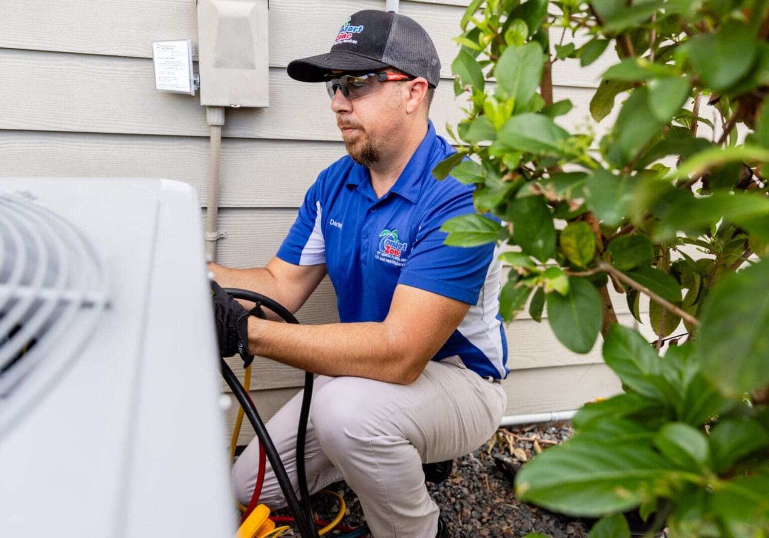 Service Technician Performing Maintenance on an Outdoor Air Conditioning Unit A service technician wearing a uniform and safety gloves is working on an outdoor air conditioning unit in a shaded backyard, using tools to inspect and repair the system