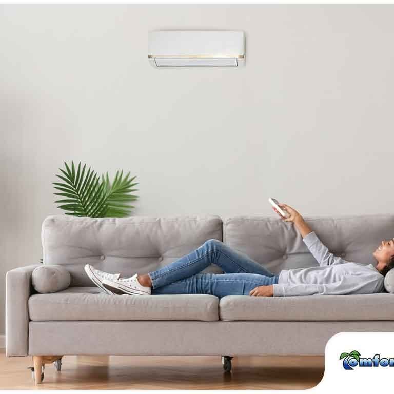 Person Relaxing on Couch in Front of Air Conditioner A person is laying on the couch in front of an air conditioner, enjoying the comfort of clean indoor air quality
