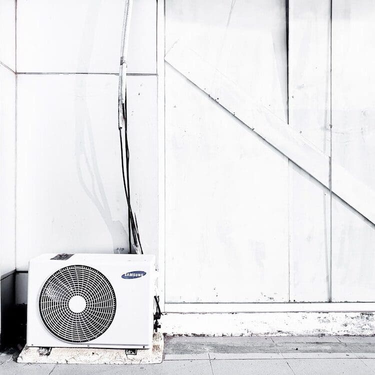 A white frozen air conditioner is sitting outside of a building, likely due to ice buildup or low temperatures affecting its operation