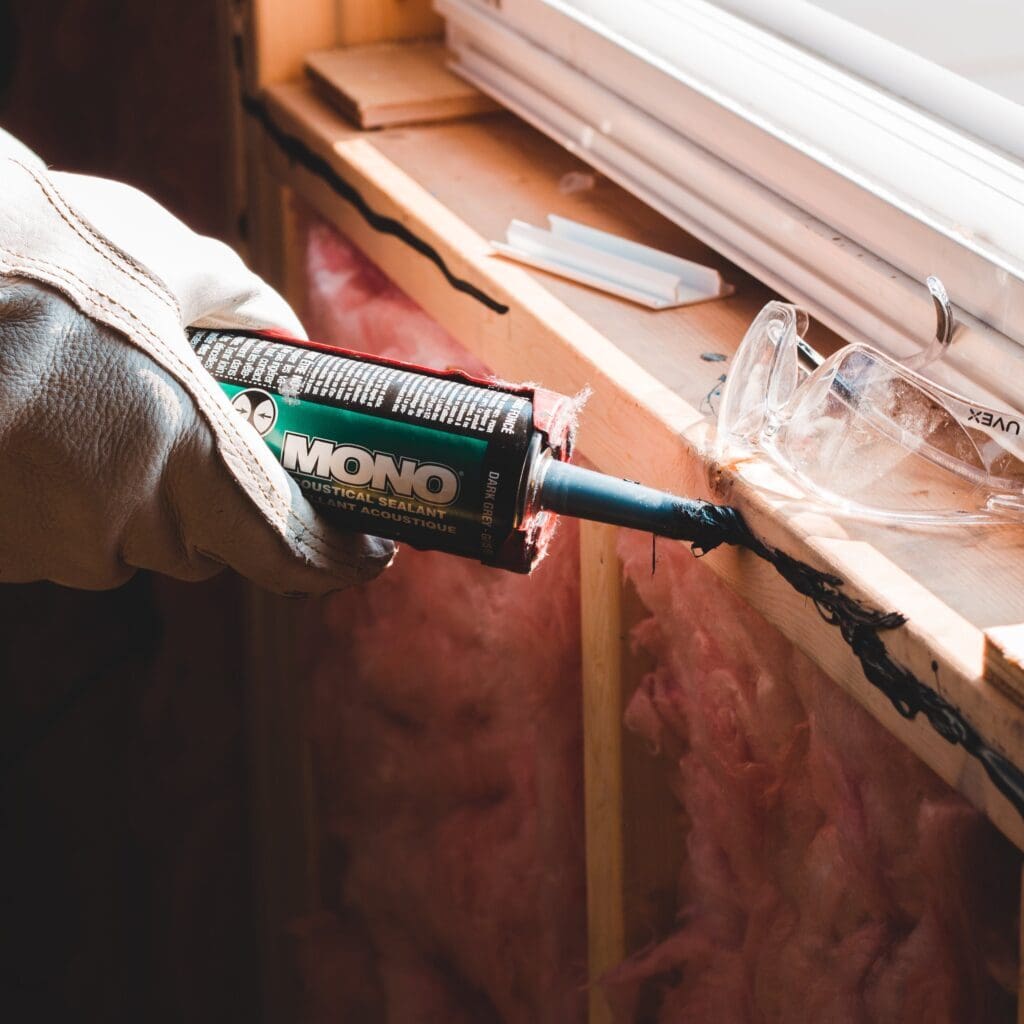 A contractor is using a glue gun next to a window to seal up air leakage, improving the home's energy efficiency