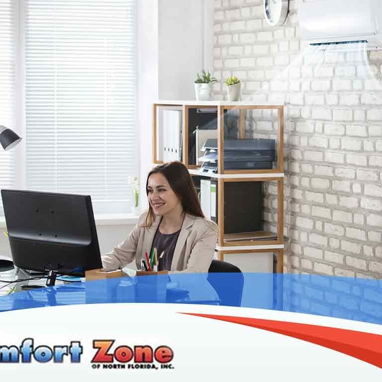 A woman is sitting at her desk with a laptop, working or browsing in a comfortable workspace
