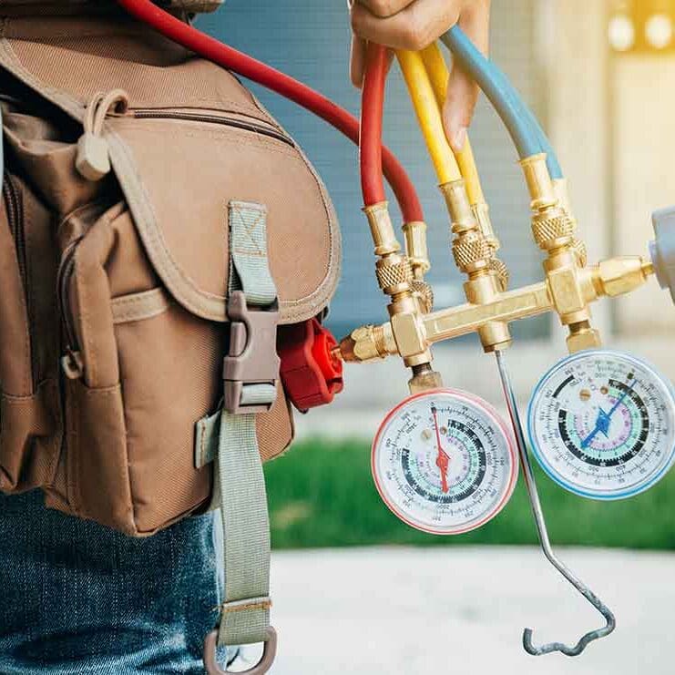 An HVAC technician is walking to service an air conditioning system, carrying gauges to check system performance and make necessary adjustments