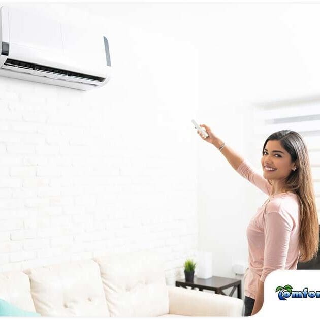 A woman is standing in front of a ductless cooling unit, smiling and happy about her new installation, enjoying the comfort of her upgraded system