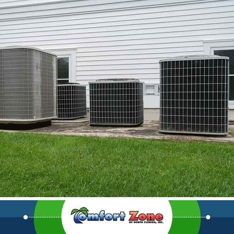 A group of air conditioning units are sitting in the grass, likely positioned for cooling purposes or awaiting installation