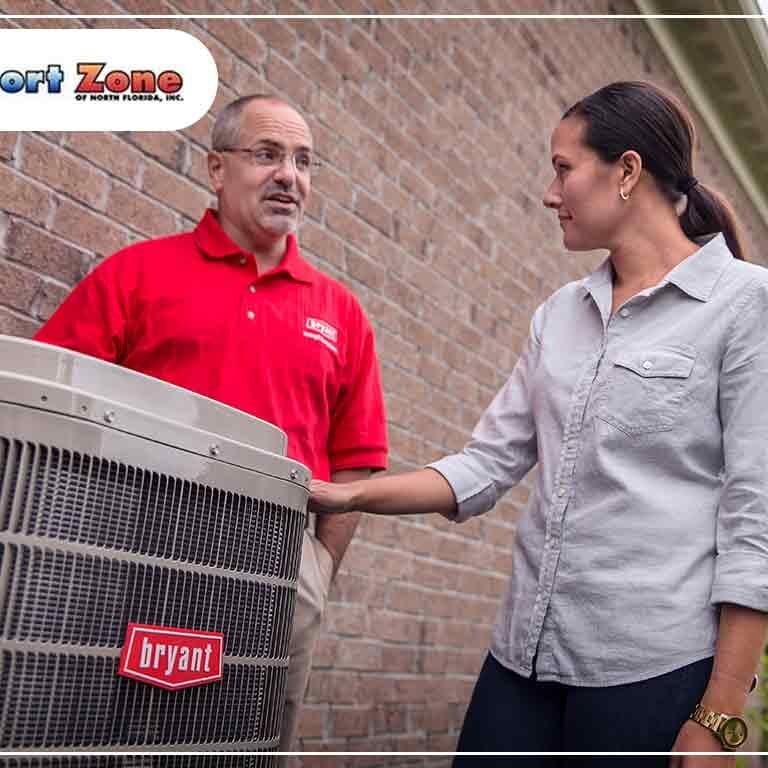 A man and woman are standing next to an air conditioner, possibly discussing its operation or maintenance.