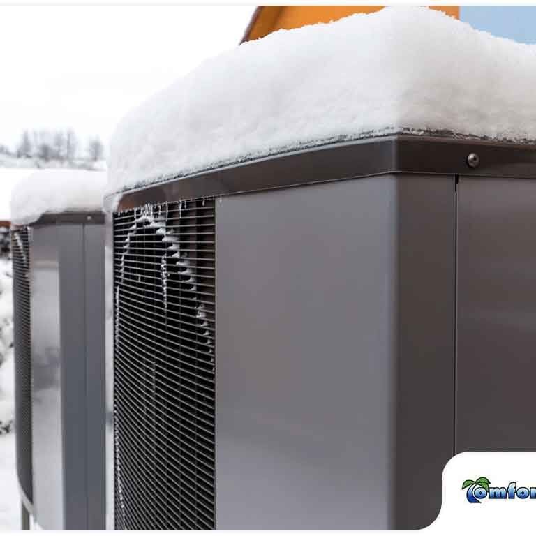 Heat Pump Air Conditioner Covered in Snow and Ice A close-up of a heat pump air conditioner unit covered in snow and ice during the winter, highlighting the effects of cold weather on HVAC systems
