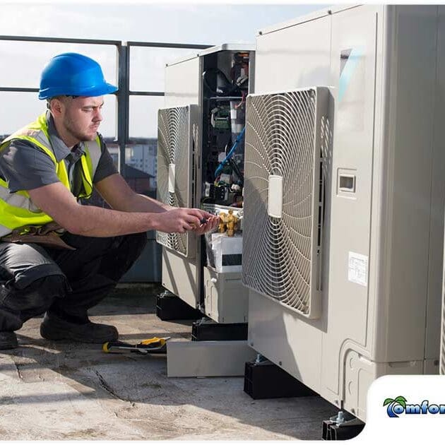 Technician in Yellow Vest and Hard Hat Fixing Air Conditioner on Roof of Residential Building A man in a yellow vest and hard hat is fixing an air conditioner on the roof of a residential building, ensuring the unit is operating properly