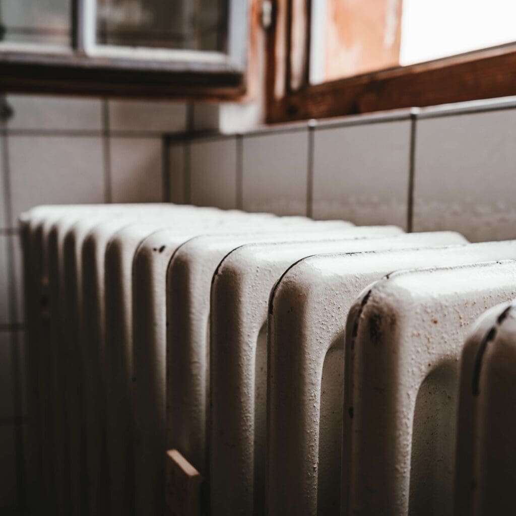 A row of white heating radiators is sitting in front of a window, providing warmth to the room during cold weather.