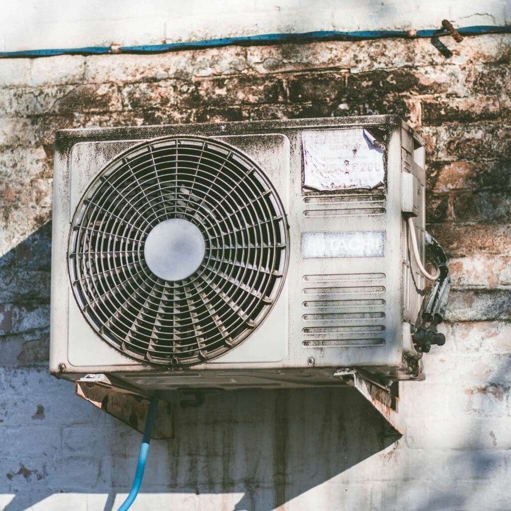 A dirty air conditioner mounted on the side of a building, with visible dirt and grime that may reduce its cooling performance